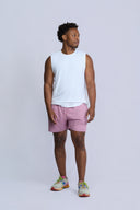 Man wearing a white sleeveless shirt and pink shorts on a light gray background