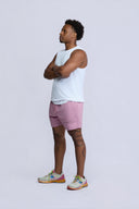 Man wearing a white tank top and pink shorts standing against a light gray background